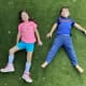 Two smiling children, a girl with cerebral palsy wearing ankle foot orthotics and a boy, lie in the grass together.